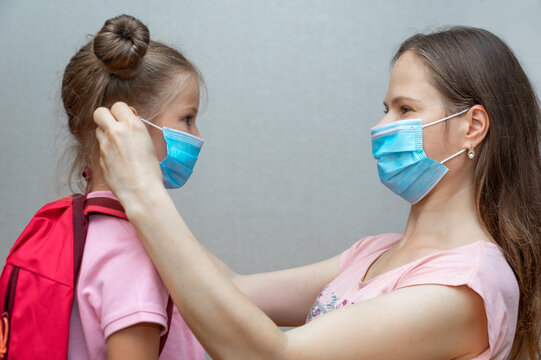 Portrait of a schoolgirl's daughter and mother in a medical mask at the door. The mother puts a sterile medical mask on the child. Back to school. Get your child to school. Social distance and safety.