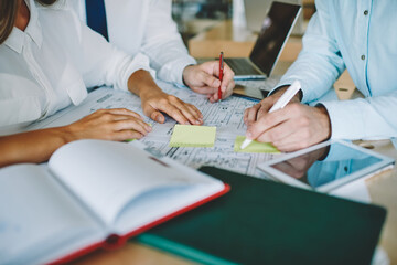 Group of male and female colleagues discussing ideas for startup project creating new architect sketches together, cropped image of crew cooperating on graphs brainstorming in company office