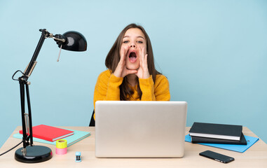 Student girl studying in her house isolated on blue background shouting and announcing something