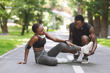 Caring Black Man Massaging Injured Leg Of Girlfriend After Running Together Outdoors