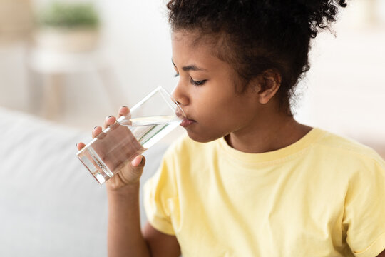 Black Kid Girl Drinking Water Sitting On Sofa At Home