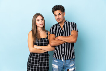 Teenager caucasian couple isolated on blue background keeping the arms crossed in frontal position