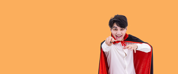Asian man wearing Halloween costume as vampire Dracula on orange background, holding magic wand,...