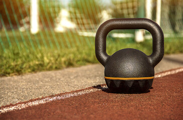 Fototapeta na wymiar Kettlebell standing on rubber coating surface of outdoor workout ground with soccer field behind