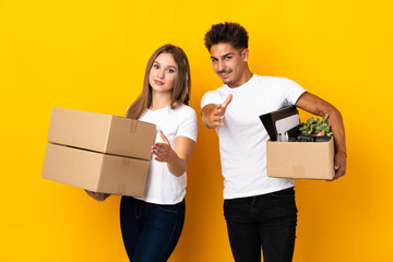Teenager couple moving in new home among boxes isolated on blue background shaking hands for...