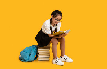 Japanese Schoolgirl Reading Book Doing Homework Sitting Over Yellow Background
