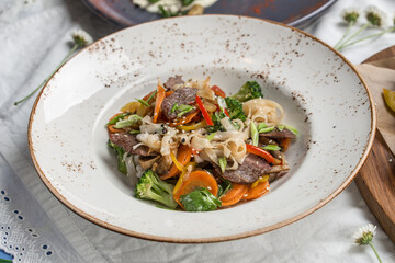 Chinese food beef noodles with broccoli, carrot, pepper and sesame seeds on the table