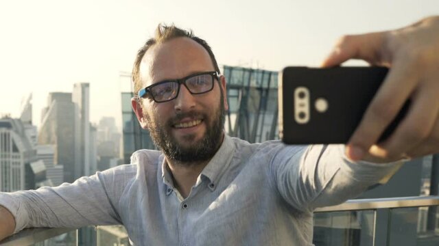 Young man taking selfie with cellphone at luxury rooftop bar during sunset