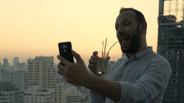 Young man taking selfie with cellphone at luxury rooftop bar
