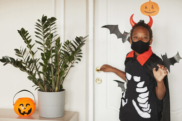Modern African American boy wearing devil costume with red horns and black mask on face saying bye...