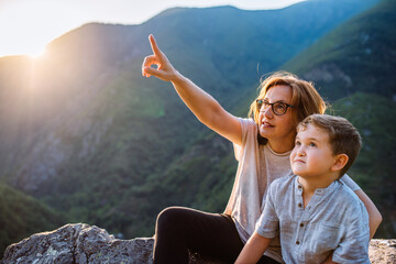 Mother and six-year-old son sitting on the mountain at sunset