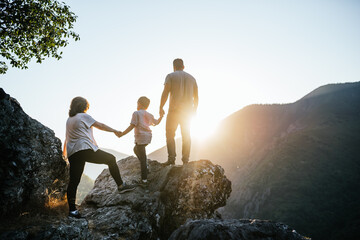 Family of a woman man and a six year old boy holding hands in silhouette at sunset on the mountain.