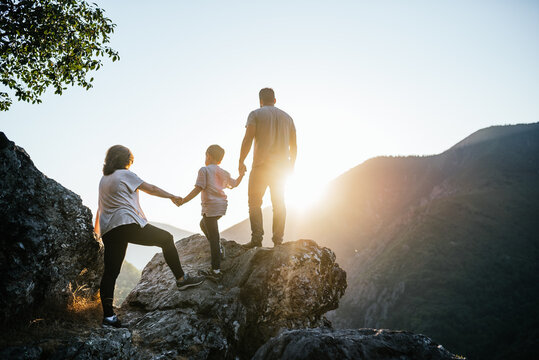 Family of a woman man and a six year old boy holding hands in silhouette at sunset on the mountain.