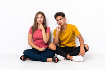 Fototapeta na wymiar Young couple sitting on the floor isolated on white background having doubts and thinking
