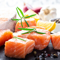 Fresh raw salmon fillet on black cutting board with lemon and spices. Healthy food concept. Close up view