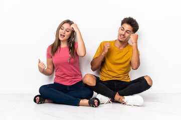 Fototapeta na wymiar Young couple sitting on the floor isolated on white background celebrating a victory