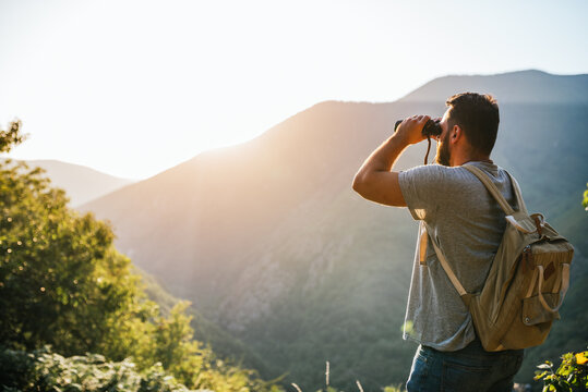 young man looking through binoculars on a mountain at sunset