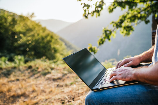 Man's hands playing the keyboard of a laptop in the mountain.Teleworking concept