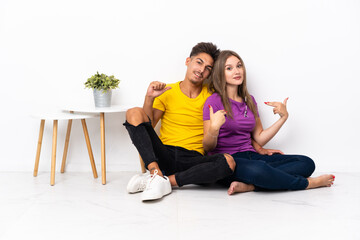 Young couple sitting on the floor isolated on white background proud and self-satisfied in love yourself concept