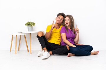 Fototapeta na wymiar Young couple sitting on the floor isolated on white background intending to realizes the solution while lifting a finger up