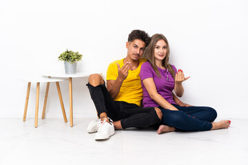 Fototapeta na wymiar Young couple sitting on the floor isolated on white background inviting to come with hand. Happy that you came