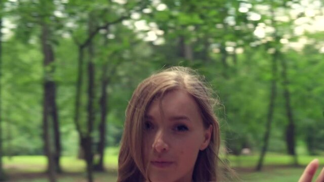 A beautiful young girl goes to a meeting and looks at the camera. The girl walks through the forest in summer. 4K video.