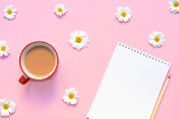 Empty notebook with coffee mug, pen, and flowers on pastel pink background. Summer or spring composition. Image with copy space, top view, flat lay