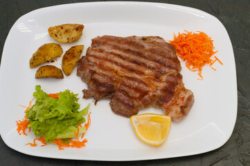 Grilled meat steak with lemon, carrots, lettuce and potatoes. Juicy and very tasty dish of Italian cuisine