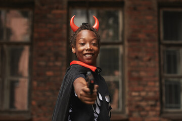 Portrait of joyful preteen boy dressed up as devil with red horns for Halloween party standing...