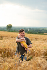 Naklejka na ściany i meble A young father holds his three month old son in his arms. Filmed in a wheat field.
