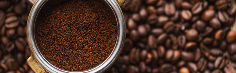 top view of ground coffee in portafilter on coffee beans background, panoramic shot