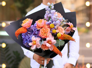 Beautiful bouquet of mixed flowers in mans hands. The work of the florist at a flower shop. Stylish...