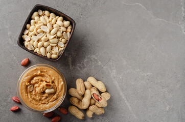 Flat lay view at glass bowl with peanut butter on stone table. Healthy eating concept