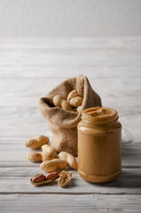 Low angle view at glass mason jar with peanut butter on white wooden table with burlap sack on backside. Healthy eating concept