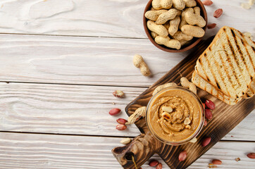 Flat lay view at glass bowl with peanut butter on cut board with toasts aside. Healthy eating concept