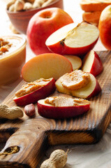 Cut board with apple slices with peanut butter on white wooden kitchen table