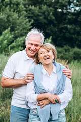 mature couple is walking with dog in park. Elderly couple resting in nature with a dog. Full-length portrait of an elderly man and woman in white shirts and jeans. Stylish and modern grandparents.