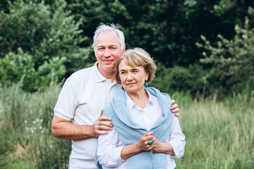 mature couple is walking with dog in park. Elderly couple resting in nature with a dog. Full-length portrait of an elderly man and woman in white shirts and jeans. Stylish and modern grandparents.