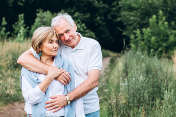 mature couple is walking with dog in park. Elderly couple resting in nature with a dog. Full-length portrait of an elderly man and woman in white shirts and jeans. Stylish and modern grandparents.