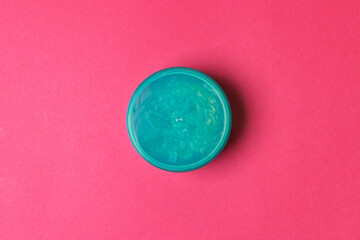 closed jar with aloe vera lotion on red colored paper background. top view