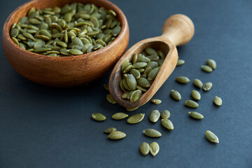 pumpkin seeds in a wooden bowl and vintage scoop. Close up on a black background. copy space for text