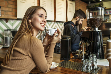 Portrait of young blonde and happy woman, customer and lady, sitting ner bar counted and drinking coffee