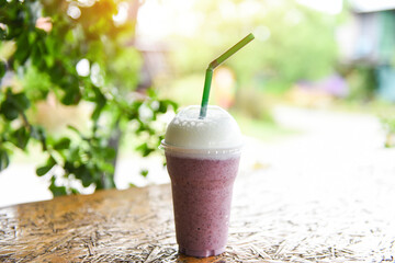 Blueberry smoothie with milk on plastic glass on the wooden table and nature green background - blueberry juice