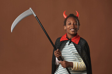 Studio portrait of cheerful African American preteen boy wearing red horns on head and costume...