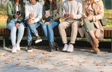 Cropped of young friends using mobile phones, sitting on bench