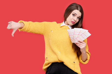 Woman showing thumb down gesture and holding lottery tickets, isolated red background
