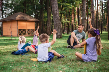 Back to school. Kindergarten and elementary scholars sitting with teacher on grass at open-air class