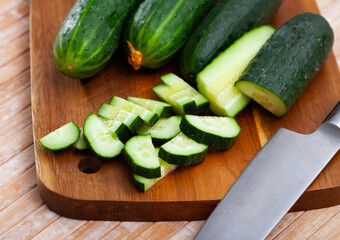 Green cucumbers sliced on wooden cutting board, food preparation