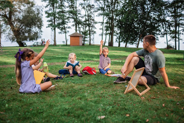 Back to school. Kindergarten and elementary scholars sitting with teacher on grass at open-air class