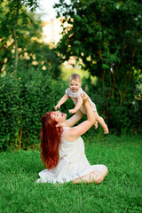 Obraz premium Mom raises her one-year-old daughter over her head in the park.